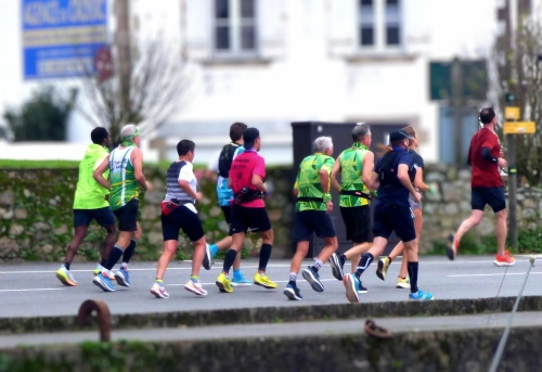 Un groupe de coureurs participant à un événement de course à pied, vu de dos, sur une route en milieu urbain.
