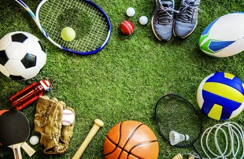 Divers équipements de sport disposés en cercle sur un terrain en gazon, comprenant un ballon de football, une raquette de tennis, des chaussures de sport, et d'autres articles sportifs.