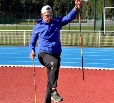 Un homme en tenue de sport effectuant un exercice d'équilibre avec des bâtons de marche nordique sur une piste d'athlétisme, dans une démarche sport-santé.