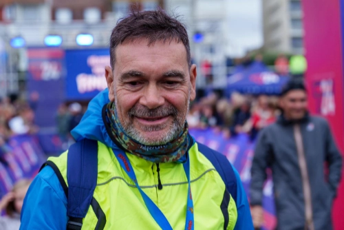 Homme souriant en veste colorée, entouré de spectateurs lors d’un événement de triathlon extrême.