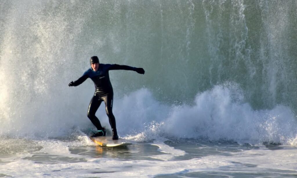 Portrait surfeur musicien : Régis sur sa planche au cœur d’une vague imposante, concentré et engagé