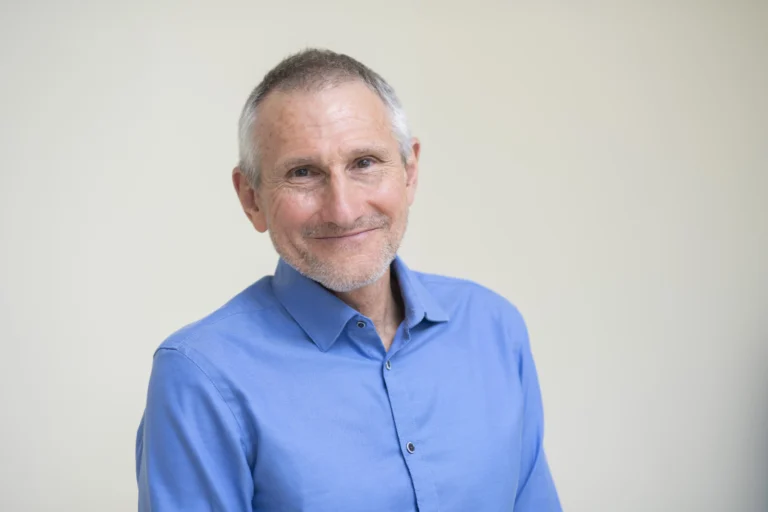 Portrait d’un homme souriant en chemise bleue, illustrant l’importance du lien entre activité physique et sédentarité chez les seniors.