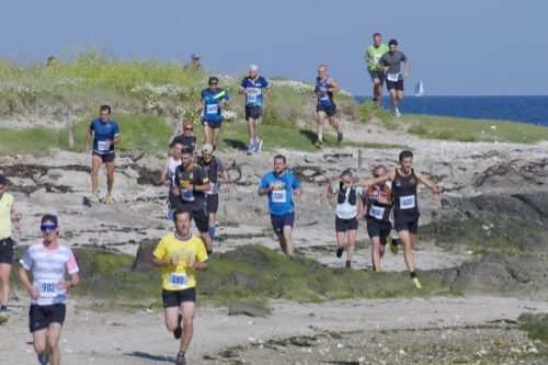 Un groupe de coureurs descend un sentier côtier rocheux lors de la course nature de Le Croisic, avec l’océan en arrière-plan.