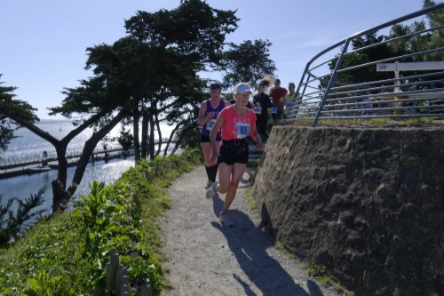 Des coureuses empruntent un sentier côtier ombragé surplombant la mer pendant la course nature de Le Croisic.