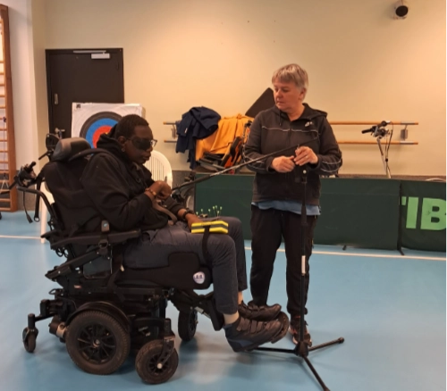 Une personne en fauteuil roulant pratique la sarbacane avec l’aide d’un encadrant dans un gymnase. Cette scène illustre l’inclusion handicap sport Le Croisic à travers une activité adaptée et accessible.