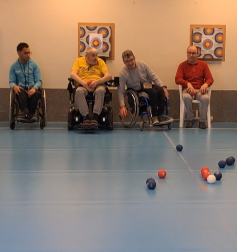 Des participants, dont plusieurs en fauteuil roulant, jouent à la boccia dans une salle du Croisic, illustrant l’inclusion handicap sport Le Croisic par une activité ludique et accessible.