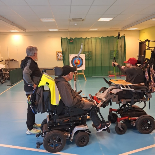 Trois personnes participent à une séance de tir à l’arc en fauteuil roulant dans un gymnase au Croisic, illustrant l’inclusion handicap sport Le Croisic à travers une activité adaptée.