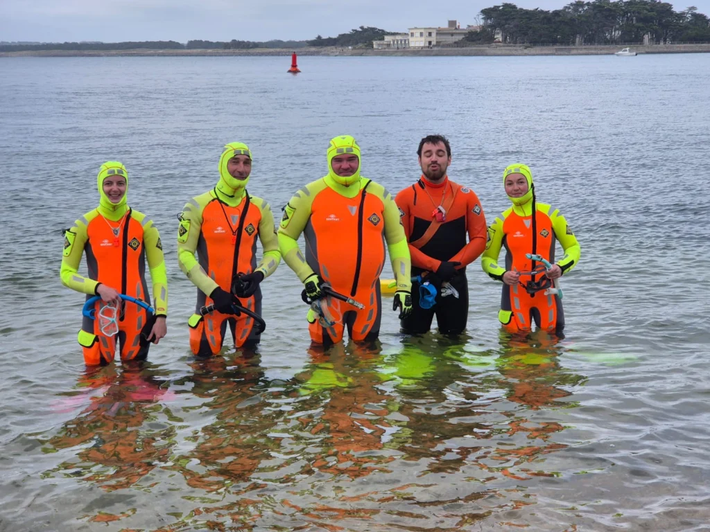 Cinq Sauveteurs-Nageurs de Bord de la SNSM en combinaison de plongée, debout dans l’eau lors d’un entraînement côtier.