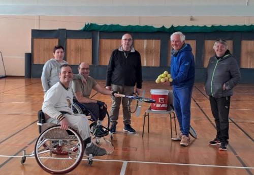 Un groupe mixte de personnes en situation de handicap et d'encadrants se réunit autour d’un entraînement de tennis en salle au Croisic, illustrant l’inclusion handicap sport Le Croisic.