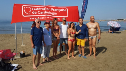 Clémence pose en maillot de bain avec un groupe de participants lors d’un événement de la Fédération Française de Cardiologie sur une plage, pour sensibiliser à la cardiomyopathie hypertrophique.