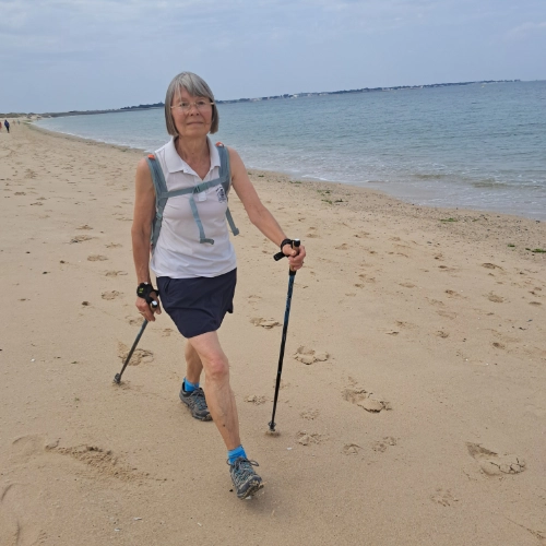 Femme senior pratiquant la marche nordique sur la plage au Croisic, illustrant une retraite active et sportive.