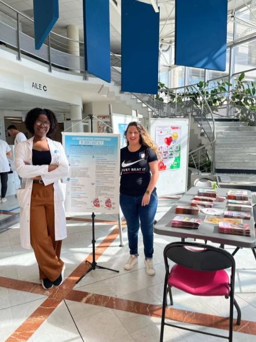 Clémence, atteinte de cardiomyopathie hypertrophique, anime un stand de sensibilisation avec une professionnelle de santé dans un hôpital.