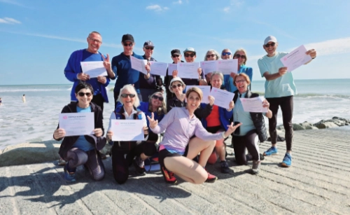 Groupe de stagiaires souriants tenant leur attestation de formation en marche nordique technique et pédagogie sur une plage ensoleillée.