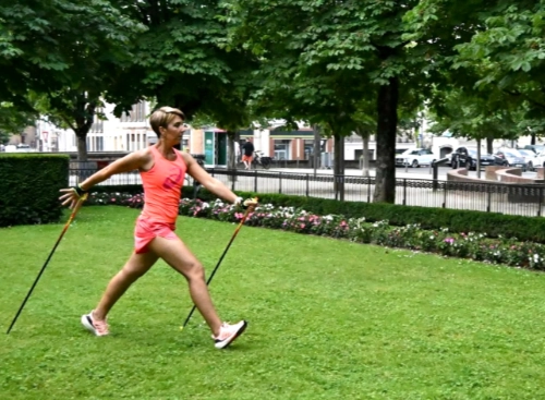Femme en pleine démonstration de marche nordique technique et pédagogie dans un parc urbain, adoptant une posture exemplaire.