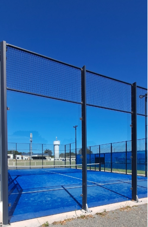 errain de padel extérieur au Croisic, avec sol bleu et clôture en verre, sous un ciel dégagé.