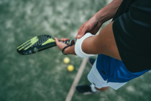 Gros plan sur un joueur de padel en plein air tenant sa raquette, prêt à servir sur un terrain synthétique.