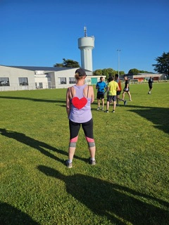 Femme de dos en tenue de sport avec un cœur rouge dessiné dans le dos, sur un terrain de course, prête à courir après un cancer dans un esprit de solidarité et de dépassement.