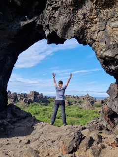 Personne debout les bras levés au milieu d’un paysage volcanique, vue à travers une arche naturelle, symbolisant la renaissance et la liberté après avoir couru après un cancer.