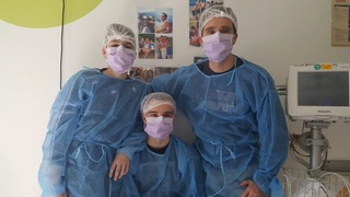 Trois jeunes en blouse et charlotte de protection posent dans une chambre d’hôpital, illustrant un engagement humain et solidaire autour du thème courir après un cancer.