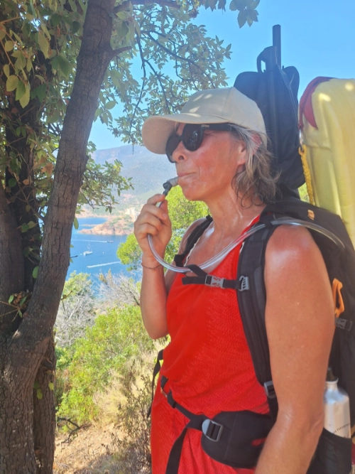 Femme en randonnée, s’hydratant avec un sac à eau sous le soleil, illustrant l’éducation corporelle pour soulager la douleur.