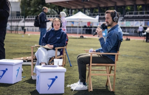 Deux personnes en plein enregistrement audio sur un terrain de sport, discutant des enjeux de l’héritage Paris 2024.
