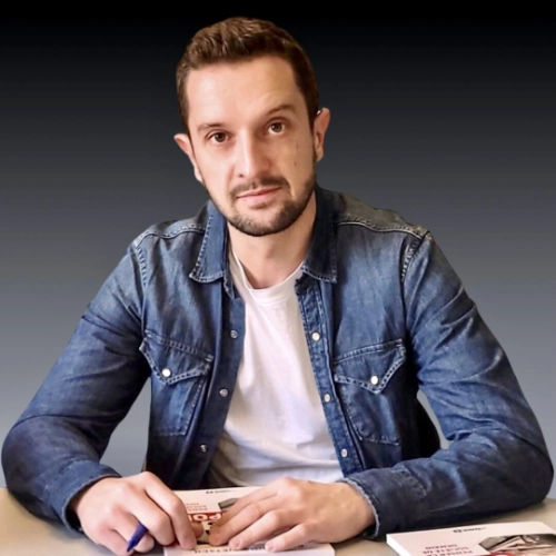 Homme assis à un bureau avec un livre sur les Jeux Olympiques, illustrant le thème de l'héritage Paris 2024.