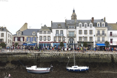 es coureurs du Marathon de la Côte d’Amour Amarris 2025 passent sur le port du Croisic, devant les maisons historiques et les bateaux.