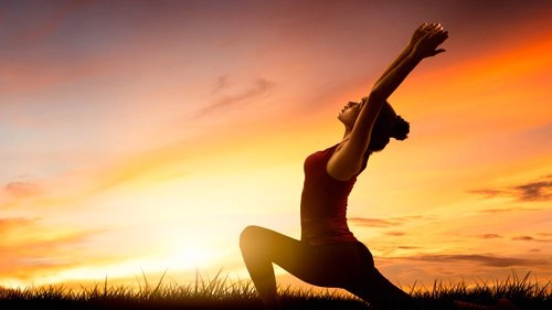 Femme pratiquant le yoga au lever du soleil pour renforcer l’équilibre intérieur et la performance sportive.