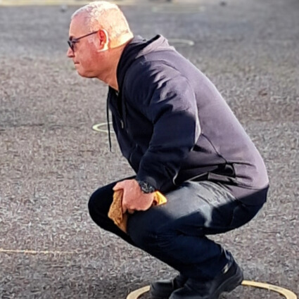 Joueur du club de pétanque du Croisic accroupi sur le terrain pendant une partie.