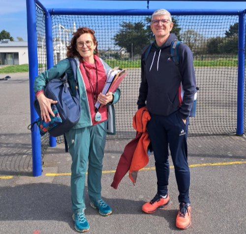 Deux adultes en tenue de sport posent devant un filet sur un terrain extérieur au lycée La Mennais de Guérande, dans le cadre de l’EPS.