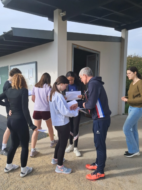 Un enseignant d’EPS échange des documents avec des élèves devant un bâtiment sportif extérieur au lycée La Mennais de Guérande.