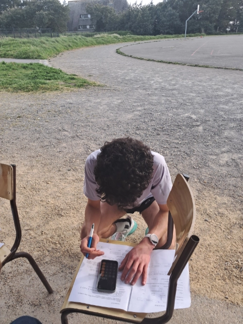 Un élève assis dehors remplit un document avec une calculatrice pendant une activité d’EPS au lycée La Mennais de Guérande.