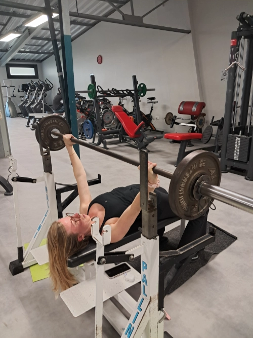 Athlète féminine en force athlétique réalisant un développé couché avec une barre chargée dans une salle de sport.