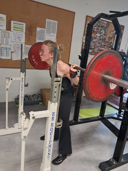 Athlète féminine en force athlétique réalisant un squat avec barre chargée sur les épaules dans une salle d’entraînement.