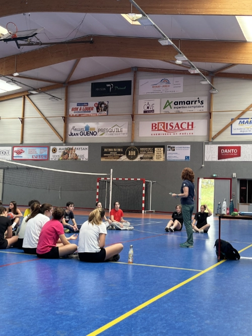 Des élèves assis dans un gymnase écoutent une intervenante lors d’une activité d’EPS au lycée La Mennais de Guérande.