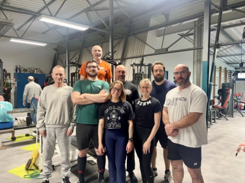 Groupe de pratiquants de force athlétique féminine et masculine posant ensemble dans une salle de sport équipée.
