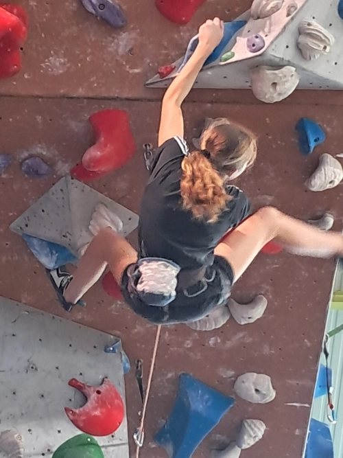 Jeune grimpeuse vue de haut sur un mur d’escalade en salle, équipée d’un baudrier dans un club d’escalade à Saint-Molf.