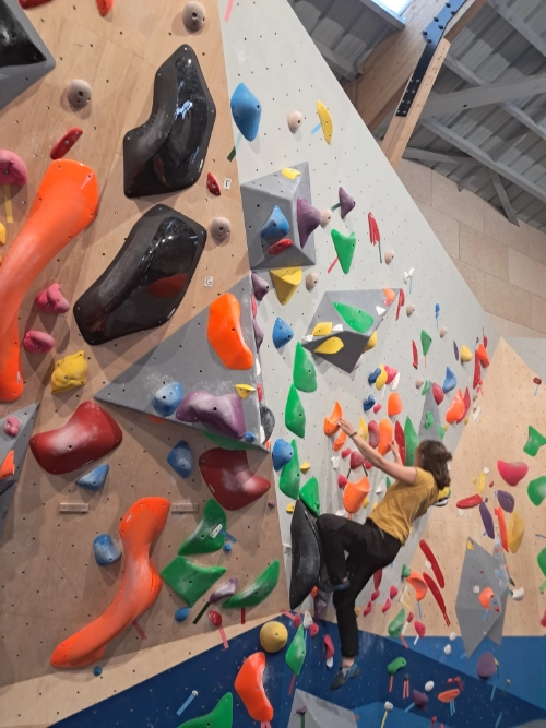 Femme grimpant sur un mur d’escalade en salle avec de nombreuses prises colorées dans un club d’escalade à Saint-Molf.