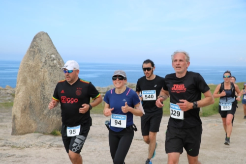 Coureurs de la Course Nature du Croisic 2026 passant devant un grand menhir avec l’océan en arrière-plan.