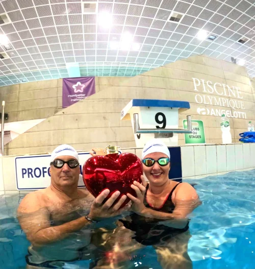 lémence nage pour sensibiliser à la cardiomyopathie hypertrophique Clémence et un nageur tiennent un cœur rouge brillant dans une piscine olympique, pour sensibiliser à la cardiomyopathie hypertrophique.